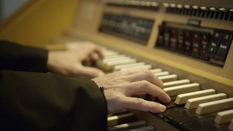 A-shot-of-man's-hands-playing-on-the-organ,-artificial-lighting,-black-and-white-keys,-wooden-casing