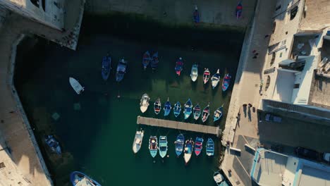 Top-down-drone-lowering-shots-of-traditional-fishing-boats-moored-in-the-Italian-city-of-Monopoli-on-a-sunny-day