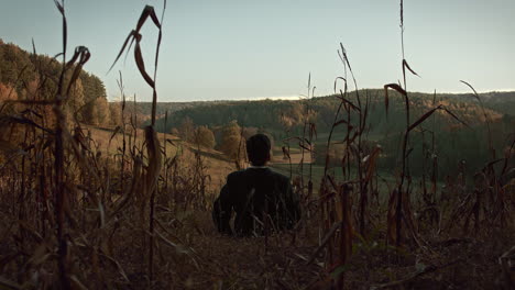 A-young-man-sits-in-the-middle-of-the-corn-field-in-late-autumn-and-lays-down-on-the-ground-to-look-at-the-sky