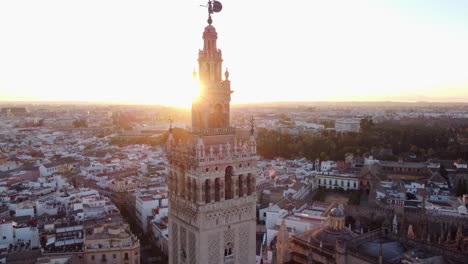 Aerial-dolly-out-revealing-Giralda-tower-in-the-famous-European-cathedral-of-Seville-with-scenic-sunlight-behind