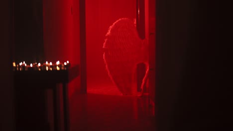 Filmische-Zeitlupenaufnahme-Einer-Bühne-Mit-Roter-Stimmungsbeleuchtung-Und-Kerzen-Auf-Einem-Tisch,-Weiße-Gefiederte-Flügel-Im-Hintergrund