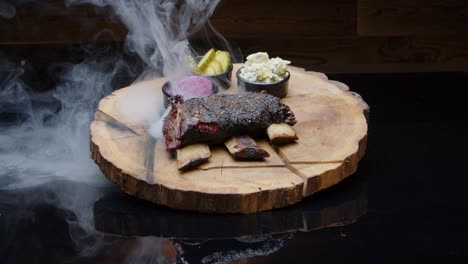 Hot-smoking-tasty-bbq-ribs-on-a-rustic-wooden-plate-with-sides-of-pickles-medium-tilt-up-shot