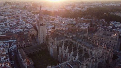 Aerial-view-over-Seville-gothic-old-town-cathedral,-Andalusia,-Sunrise-across-Spanish-landmark,-Orbiting-pull-back