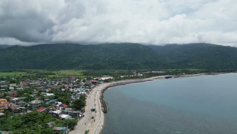 Aerial,-Rising-Shot-of-Wide-Bay-and-Seawall-near-Coastal-Town-of-Virac,-Catanduanes,-Philippines,-Asia-with-Mountains-in-background