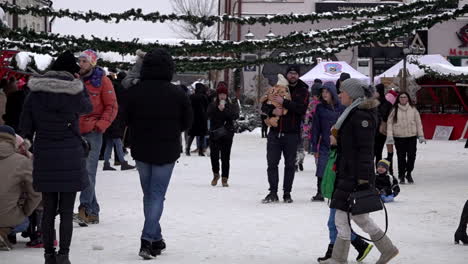 In-slow-motion-men,-women-and-children-attend-a-Christmas-fair-of-festive-stalls-in-a-snow-covered-town-square