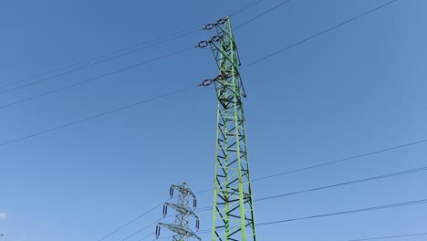 Panning-shot-revealing-green-electric-pylon-with-high-voltage-wires-to-transmit-electricity-on-long-distances