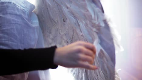 Cinematic-slow-motion-shot-of-a-person-with-feathered-wings-and-a-woman-touching-the-feathers-with-her-hand