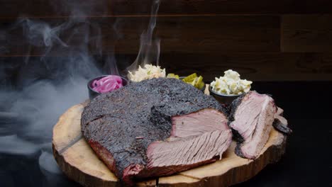 Perfectly-grilled-pork-ham-on-a-rustic-wooden-plate-with-sides-and-with-a-smoking-background---tilt-up-medium-shot