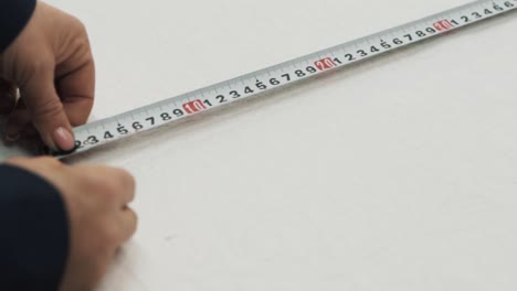 Close-up-of-female-hands-measuring-with-a-pencil-on-white-fabric-using-a-ruler-in-a-textile-factory