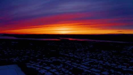 Aerial-drone-view-of-a-vivid,-blazing-sunset-over-a-snowy-residential-neighborhood