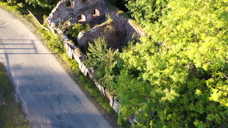 Asphalt-road-and-derelict-stone-farm-building,-aerial-ascend-view