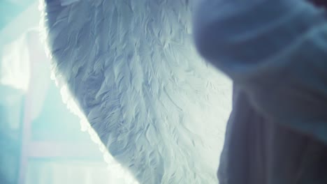 Close-up-of-a-person-with-white-angel-wings-on-his-back-while-a-magical-light-enters-the-room