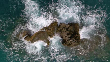 Aerial,-top-down-view-of-sea-water-washing-rocks,-flying-up-vertical-in-240fps-slow-motion