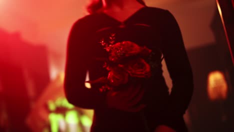 medium-shot-of-a-woman-holding-a-bouquet-of-roses-seductively-in-a-house-with-red-light