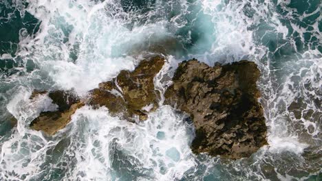 Aerial,-top-down,-close-up-view-of-sea-water-washing-rocks-in-240fps-slow-motion