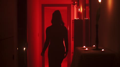 Cinematic-slow-motion-shot-of-a-woman-walking-seductively-into-a-room-on-a-stage-with-red-mood-lighting-and-burning-candles