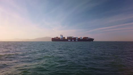 Gimbal-wide-static-shot-of-an-MSC-container-ship-passing-by-to-reveal-Alcatraz-Island-from-San-Francisco,-California