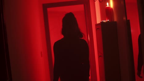 Black-silhouette-of-a-curvy-woman-walking-with-her-back-to-the-camera-in-a-corridor-with-a-red-low-light-environment