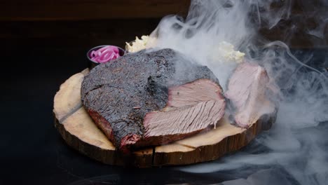 Perfectly-grilled-pork-ham-on-a-rustic-wooden-plate-with-sides-covered-with-a-thick-cloud-of-smoke---tilt-up-medium-shot