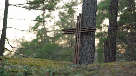 Wooden-cross-leaning-against-a-tree-in-a-forest-in-the-evening
