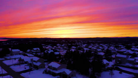 Aerial-view-of-a-stunningly-beautiful-winter-sunset-over-a-snow-covered-residential-neighborhood