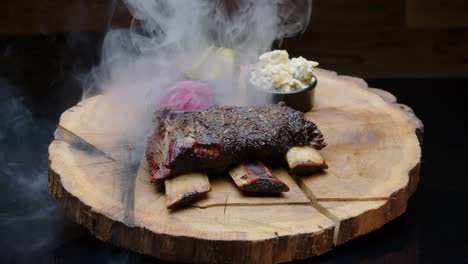 BBQ-ribs-on-a-rustic-wooden-plate-with-pickles-covered-with-a-cloud-of-smoke---medium-shot