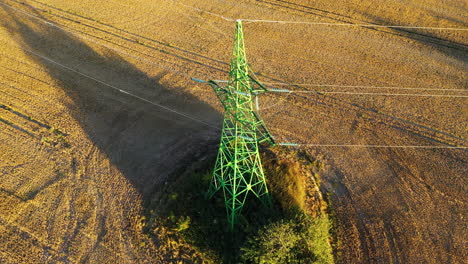 High-voltage-electricity-tower-in-rural-field,-power-supply-to-countryside-village,-drone-view