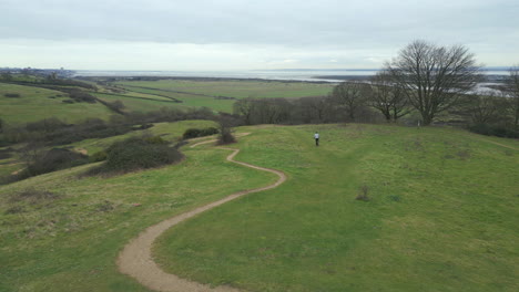 Mountain-biker-riding-over-hill-approaching-rocky-trail-at-Hadleigh-Park,-drone