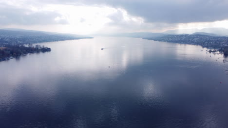 Aerial-tilt-up-over-a-single-boat-sailing-Zurich-lake-in-Switzerland-on-a-cloudy-day