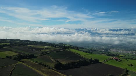 Drone-gimbal-down-revealing-green-rural-agricultural-field-in-Costa-Rica-above-the-clouds