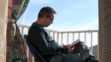 Adult-man-reading-a-book-on-the-balcony-at-home-on-a-sunny-day