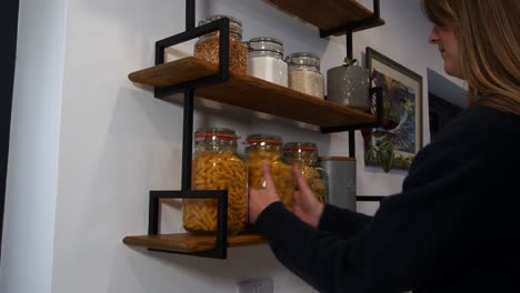 Female-model-choosing-then-taking-a-jar-of-pasta-from-kitchen-shelves-in-a-kitchen