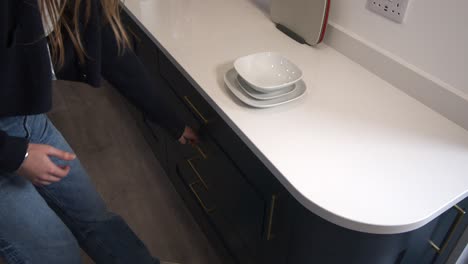 female-model-opening-kitchen-drawers-and-placing,-putting-in-dinner-plate,-side-plate-and-breakfast-bowl-and-walking-off-in-a-modern-kitchen