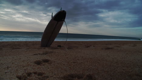 Standing-surfboard-on-sand-beach,-ocean-waves-in-background,-copyspace-or-titles-space