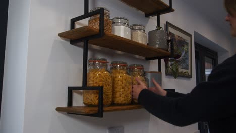Female-model-taking-a-jar-of-pasta-from-kitchen-shelves-in-a-kitchen