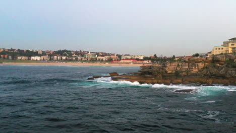 Drone-flying-over-the-rocks-in-North-Bondi-towards-the-beach,-Sydney-Australia