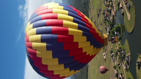 Vertikaler-Drohnenschuss,-Heißluftballons-Fliegen-über-Grüner-Landschaft-Und-See-An-Sonnigen-Sommertagen
