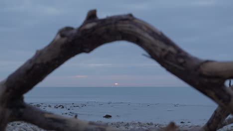 captured-through-weathered,-rustic-wooden-frame-rising-sun-casts-a-stunning-glow-over-the-calm-sea-during-morning-hours
