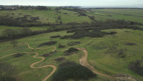 Mountain-biker-riding-along-winding-downhill-trail-at-Hadleigh-Park,-drone
