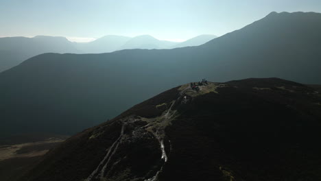 Hikers-on-mountain-summit-with-panoramic-reveal-of-misty-mountains-in-English-Lake-District-UK