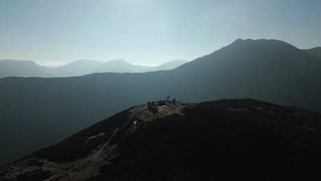 Hikers-on-mountain-summit-with-pull-back-revealing-panoramic-view-of-misty-mountains-in-English-Lake-District-UK