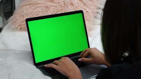 Mujer-Escribiendo-En-Una-Laptop-Con-Pantalla-Verde-Mientras-Está-Acostada-En-La-Cama,-Blogueando-O-Programando-Concepto