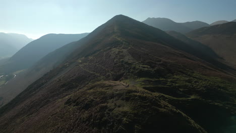 Flying-over-mountain-path-towards-summit-with-misty-mountains-beyond-in-English-Lake-District-UK