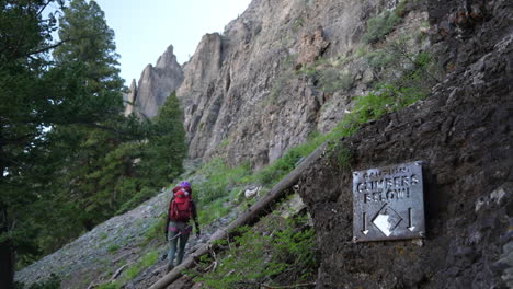 Female-Climber-on-Via-Ferrata-Route-in-Telluride-Colorado-USA-Passing-Cimbers-Below-Sign,-Back-View,-Slow-Motion