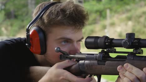 Closeup-Of-A-Man-In-Earmuffs-Aiming-On-Target-By-Looking-On-Magnification-Scope-Of-Shotgun-At-Firing-Range