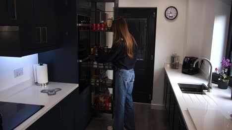 female-model-taking-a-jar,-food-out-of-a-pull-out-larder-in-a-modern-kitchen