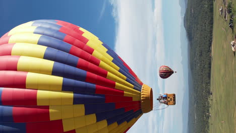 Vertikale-Luftaufnahme-Eines-Farbenfrohen-Heißluftballons,-Der-An-Einem-Sonnigen-Tag-über-Der-Landschaft-Fliegt