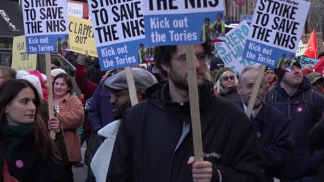 In-slow-motion-supporters-join-striking-National-Health-Service-staff-and-march-holding-“Strike-To-Save-The-NHS”-placards-on-a-protest-for-increased-pay-and-better-working-conditions