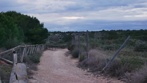 Timelapse-and-zoom-out-showing-grey-clouds-over-a-solitary-trail-next-to-a-fence