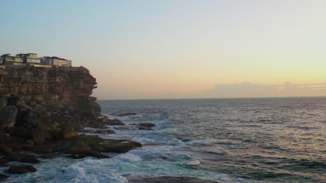 Stationary-drone-shot-of-waves-hitting-the-North-Bondi-Ben-Buckler-rocks-during-sunrise-in-Sydney,-Australia